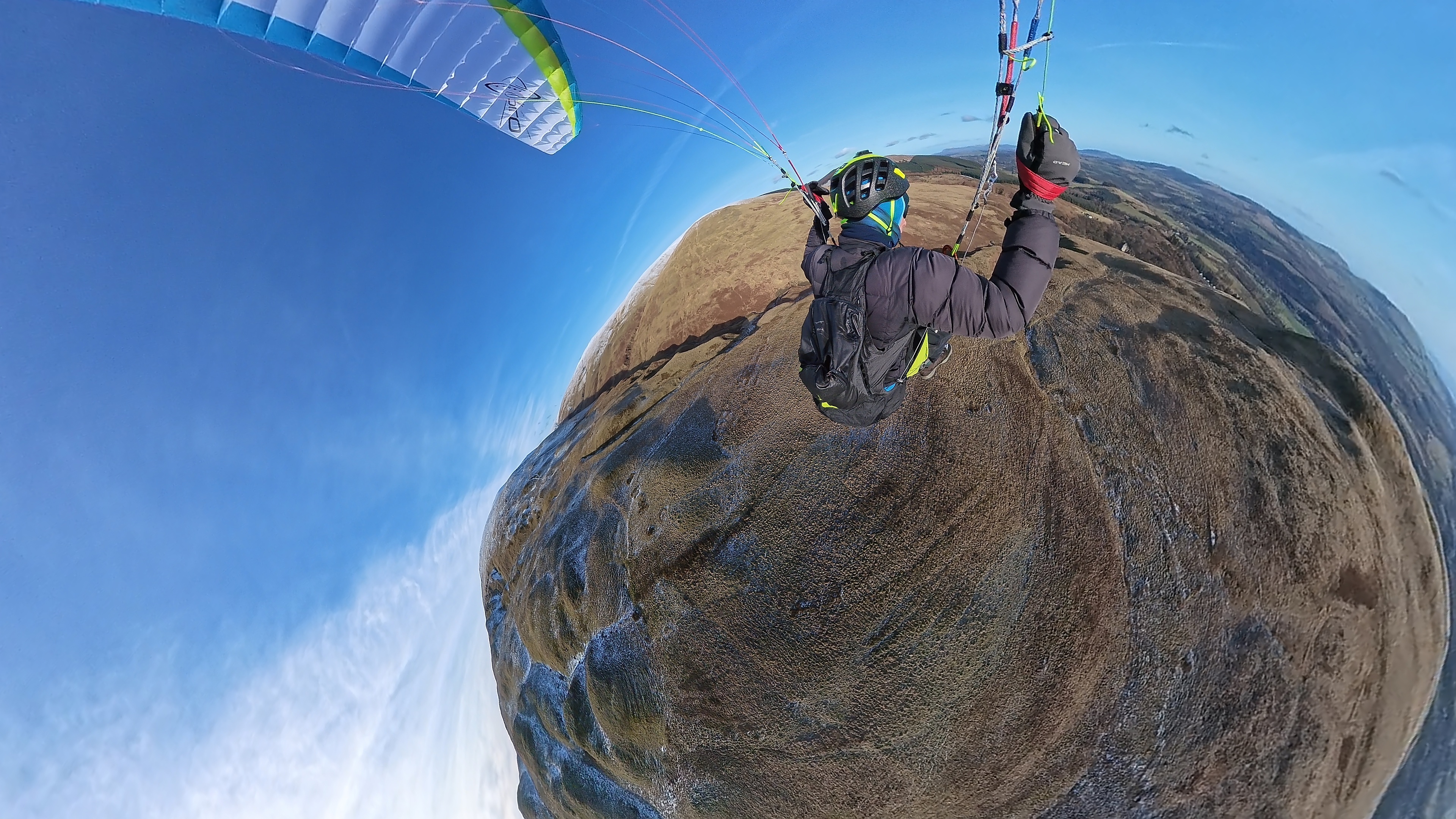 Paraglider flying high over a rounded hillside.